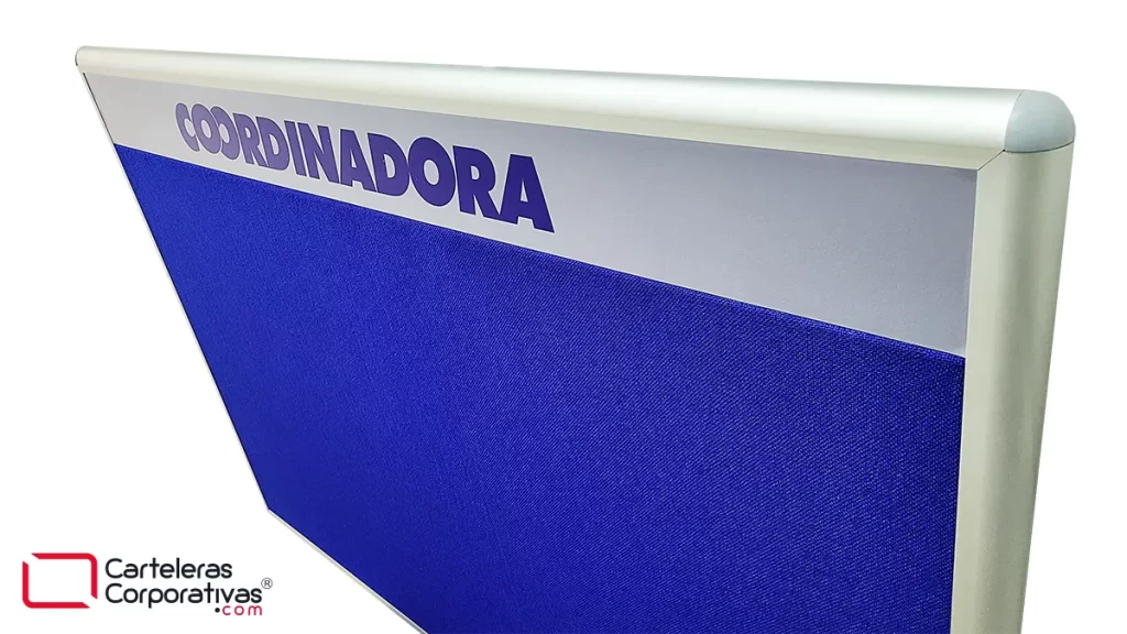 cartelera en corcho forrado en paño color azul vista esquina donde se aprecia el detalle de la esquinera plástica, el marco y la cenefa con logotipo